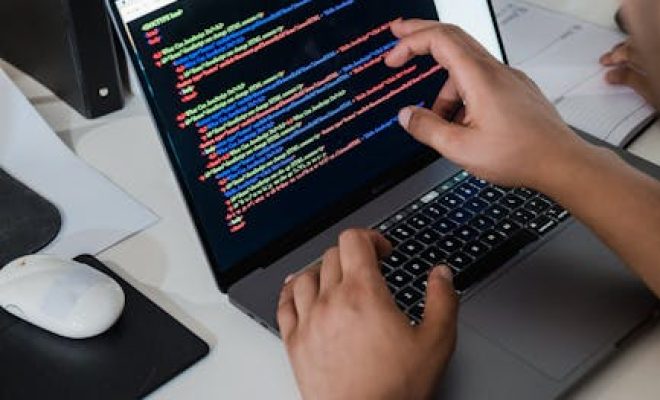 Close-up of a programmer pointing at a colorful code script on a laptop in an office setting.
